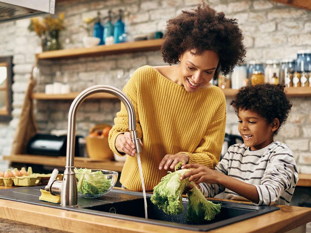 Happy African American boy with  other washing salad while preparing food in the kitchen.